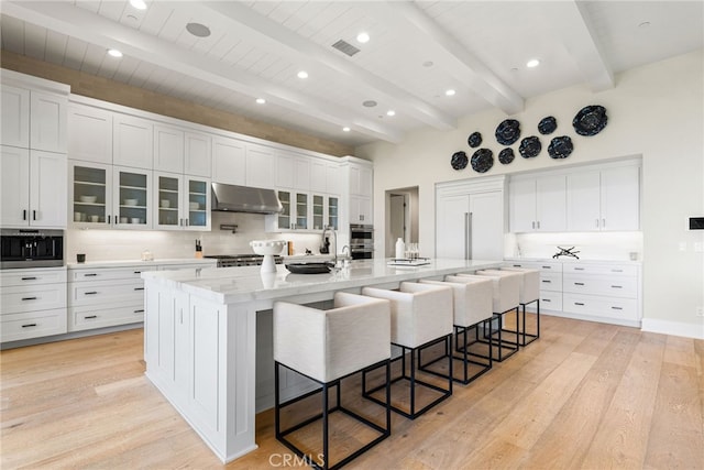 30 Catalina Vista Rd, Ladera Ranch, CA 92694 - kitchen with under cabinet range hood, a kitchen bar, light wood-style flooring, decorative backsplash, and white cabinets