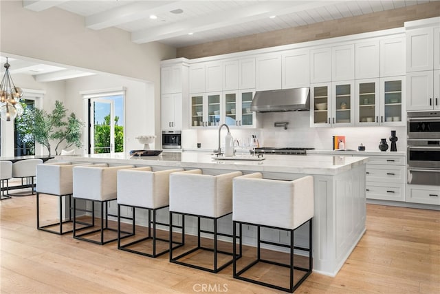 30 Catalina Vista Rd, Ladera Ranch, CA 92694 - kitchen with under cabinet range hood, beamed ceiling, a warming drawer, white cabinets, and tasteful backsplash