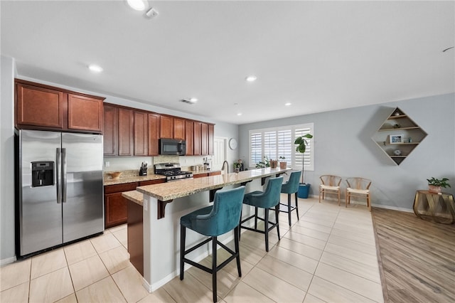 4040 Quartzite Ln, San Bernardino, CA 92407 - kitchen featuring appliances with stainless steel finishes, an island with sink, a kitchen bar, light stone countertops, and light tile patterned floors
