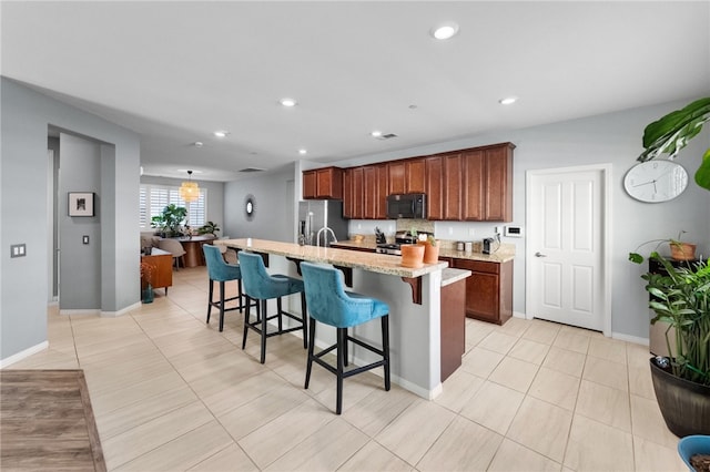 4040 Quartzite Ln, San Bernardino, CA 92407 - kitchen with stainless steel appliances, a kitchen bar, an island with sink, light stone counters, and light tile patterned floors