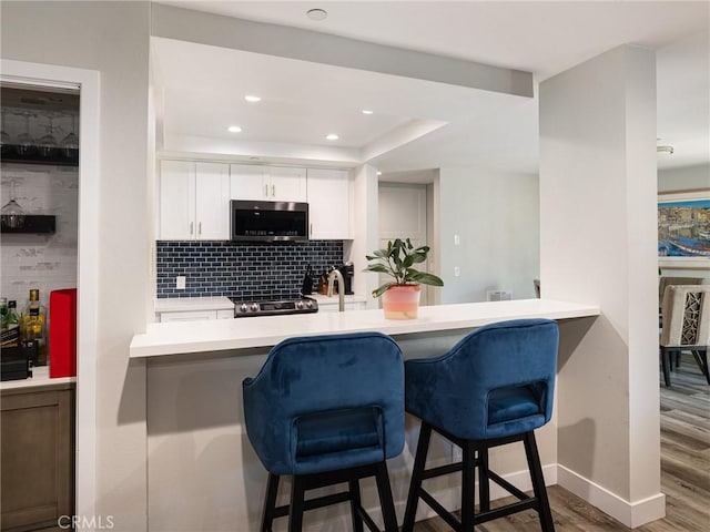 625 Esplanade Unit 29, Redondo Beach, CA 90277 - kitchen featuring stainless steel microwave, wood finished floors, backsplash, white cabinetry, and a kitchen bar