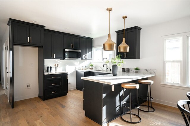2342 S Cochran Ave, Los Angeles, CA 90016 - kitchen featuring stainless steel microwave, a peninsula, dark cabinets, a kitchen bar, and light wood-style floors