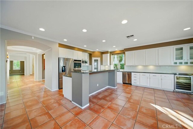 4451 Birdie Dr, Corona, CA 92883 - kitchen with wine cooler, appliances with stainless steel finishes, arched walkways, light tile patterned floors, and white cabinetry