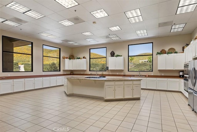 29530 Winding Brook Dr, Menifee, CA 92584 - kitchen featuring a kitchen island, white cabinetry, light tile patterned floors, a drop ceiling, and light stone counters