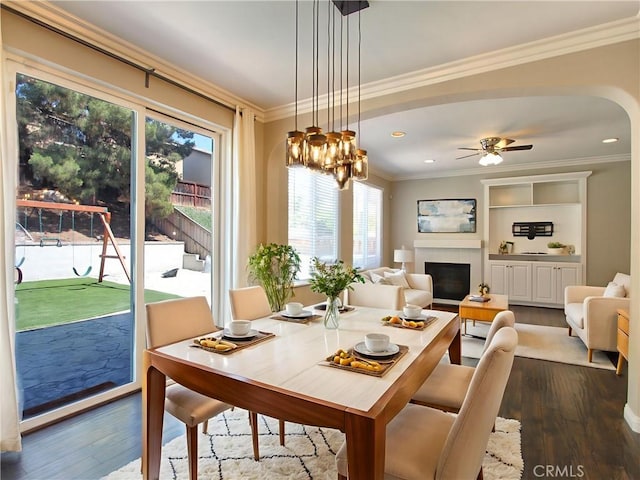 11961 Limestone Ct, Yucaipa, CA 92399 - dining space featuring dark wood-type flooring, plenty of natural light, crown molding, a glass covered fireplace, and arched walkways