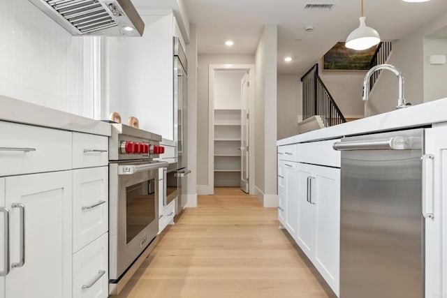3584 Garfield St, Carlsbad, CA 92008 - kitchen with appliances with stainless steel finishes, exhaust hood, white cabinets, light wood-style flooring, and decorative light fixtures