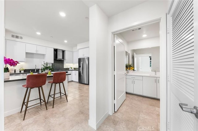 2526 Nolita, Irvine, CA 92612 - kitchen with wall chimney exhaust hood, stainless steel refrigerator with ice dispenser, white cabinetry, recessed lighting, and a kitchen bar