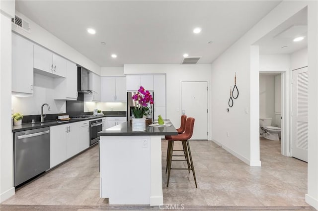 2526 Nolita, Irvine, CA 92612 - kitchen featuring stainless steel appliances, wall chimney exhaust hood, dark countertops, white cabinets, and a kitchen breakfast bar