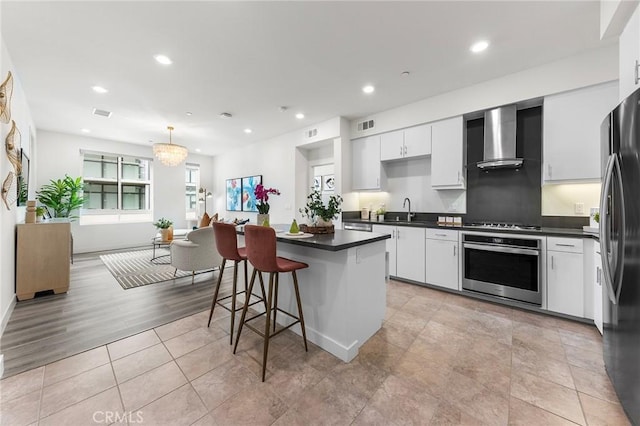 2526 Nolita, Irvine, CA 92612 - kitchen featuring appliances with stainless steel finishes, wall chimney exhaust hood, dark countertops, a kitchen island, and white cabinetry