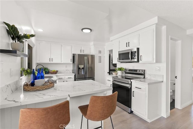 11338 Grand Manan Dr, Cypress, CA 90630 - kitchen with appliances with stainless steel finishes, a peninsula, light wood-style floors, a breakfast bar area, and white cabinets