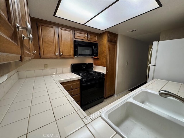 600 Central Ave Unit 323, Riverside, CA 92507 - kitchen with black appliances, tile countertops, light tile patterned flooring, and brown cabinets