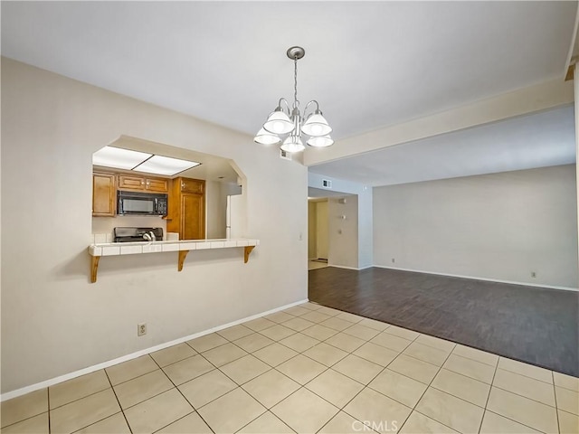 600 Central Ave Unit 323, Riverside, CA 92507 - kitchen featuring black microwave, tile countertops, brown cabinetry, a kitchen breakfast bar, and light tile patterned flooring