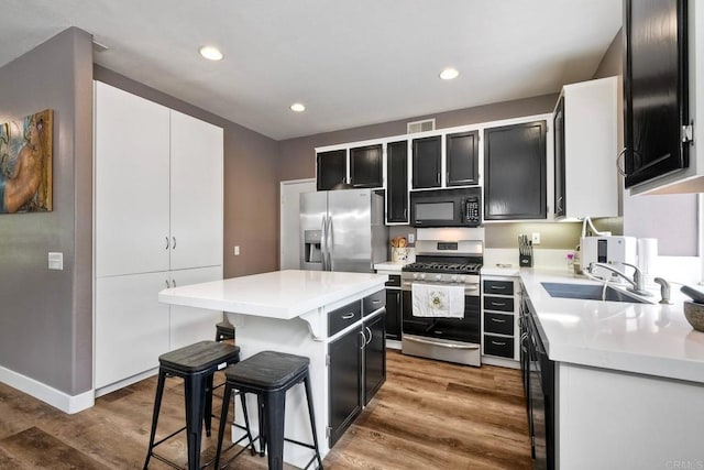 339 Diamante Way, Oceanside, CA 92056 - kitchen with appliances with stainless steel finishes, dark cabinetry, a kitchen bar, wood finished floors, and a kitchen island