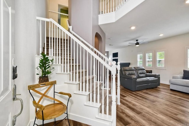 339 Diamante Way, Oceanside, CA 92056 - staircase featuring a ceiling fan, wood finished floors, arched walkways, a fireplace, and a towering ceiling