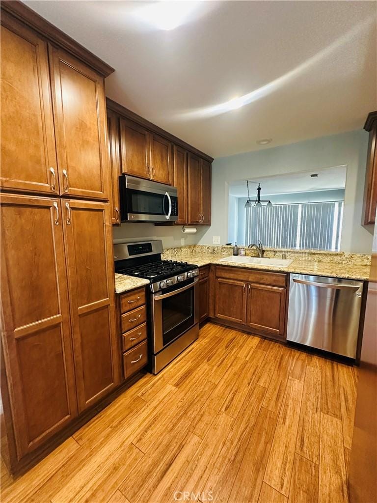 4674 Maxwell Ct, Riverside, CA 92501 - kitchen featuring appliances with stainless steel finishes, light wood-type flooring, light stone countertops, brown cabinets, and a chandelier