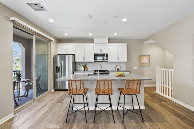 109 Alder Rdg, Lake Forest, CA 92610 - kitchen with stainless steel appliances, a center island with sink, decorative backsplash, light wood-style flooring, and white cabinetry