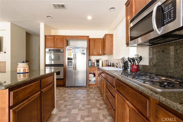 2207 Rockrose St, Palmdale, CA 93551 - kitchen with stainless steel appliances, brown cabinets, dark stone countertops, decorative backsplash, and recessed lighting