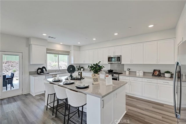 17148 Kent St, Hesperia, CA 92345 - kitchen with appliances with stainless steel finishes, a breakfast bar area, a center island, white cabinets, and light wood-style floors