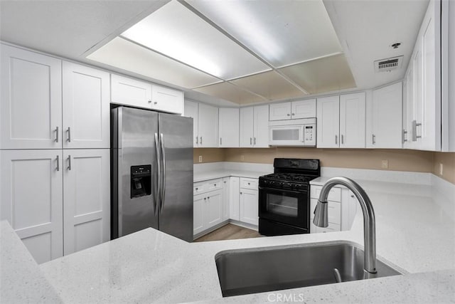 43195 Andrade Ave Unit K, Hemet, CA 92544 - kitchen with stainless steel fridge, white microwave, black range with gas stovetop, light stone countertops, and white cabinetry