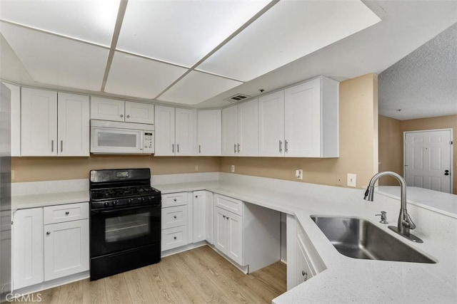 43195 Andrade Ave Unit K, Hemet, CA 92544 - kitchen with white microwave, gas stove, light wood-style flooring, white cabinets, and a peninsula