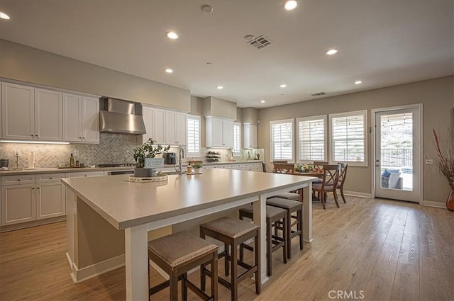 13471 Planet Ct, Riverside, CA 92503 - kitchen featuring wall chimney range hood, a kitchen island with sink, tasteful backsplash, light countertops, and recessed lighting