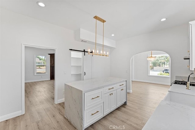 12887 Mount Vernon Ave, Grand Terrace, CA 92313 - kitchen featuring a barn door, white cabinetry, light wood-type flooring, hanging light fixtures, and arched walkways