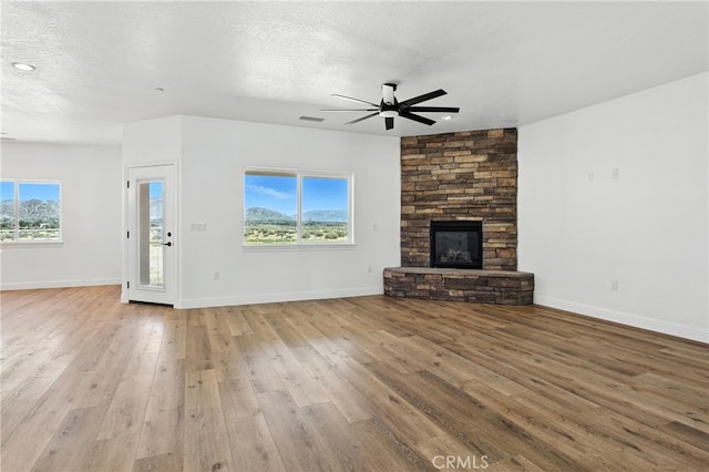 15323 Turquoise Rd, Apple Valley, CA 92307 - unfurnished living room featuring a ceiling fan, a stone fireplace, wood-type flooring, and a textured ceiling