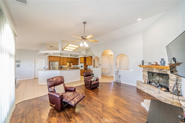 8225 Ailanthus St, Phelan, CA 92371 - living area with arched walkways, a ceiling fan, a stone fireplace, light wood finished floors, and high vaulted ceiling