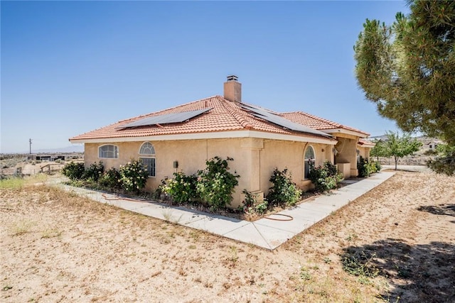 8225 Ailanthus St, Phelan, CA 92371 - view of home's exterior with stucco siding, roof mounted solar panels, a chimney, and a tile roof