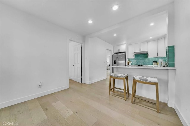 569 Lewis Ave, San Leandro, CA 94577 - kitchen featuring decorative backsplash, white cabinetry, a peninsula, light wood-style flooring, and under cabinet range hood