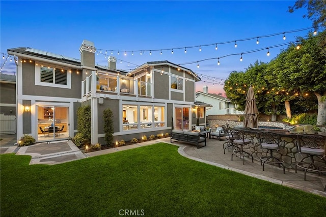 5210 Avenida De Kristine, Yorba Linda, CA 92887 - back of house at dusk featuring stucco siding, a chimney, a lawn, a patio, and roof mounted solar panels