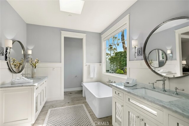 1456 Key Vw, Corona Del Mar, CA 92625 - bathroom with a wainscoted wall, a freestanding tub, two vanities, wood finished floors, and a skylight