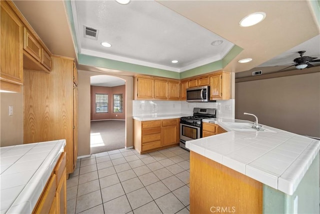 5715 Malaga Ct, Palmdale, CA 93552 - kitchen with appliances with stainless steel finishes, arched walkways, a raised ceiling, tile counters, and a peninsula