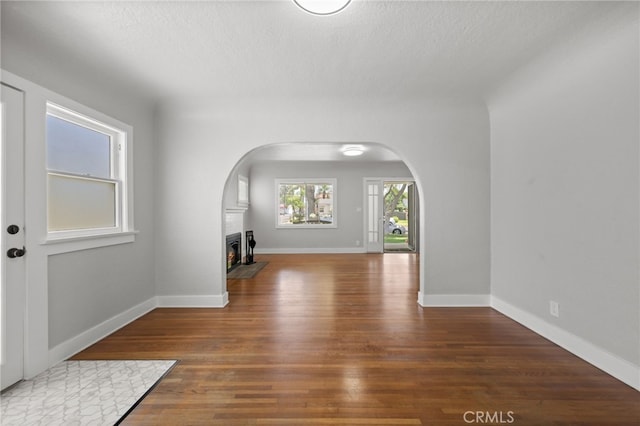 12950 7th St, Chino, CA 91710 - empty room featuring arched walkways, wood finished floors, a lit fireplace, and a textured ceiling