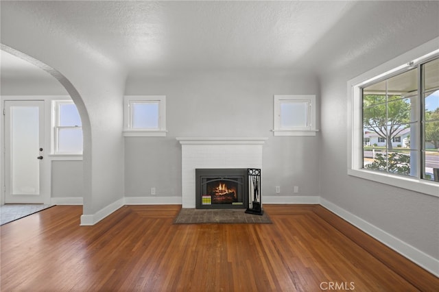 12950 7th St, Chino, CA 91710 - unfurnished living room with a brick fireplace, wood finished floors, arched walkways, and a textured ceiling