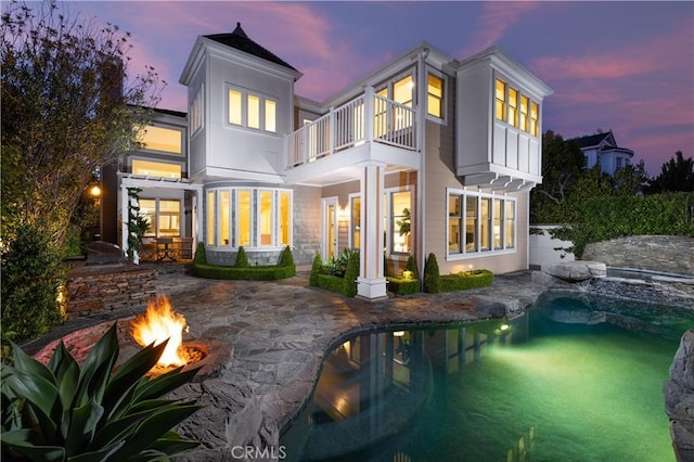 57 Cape Andover, Newport Beach, CA 92660 - back of property at dusk with a balcony, a fire pit, a patio area, and an outdoor pool