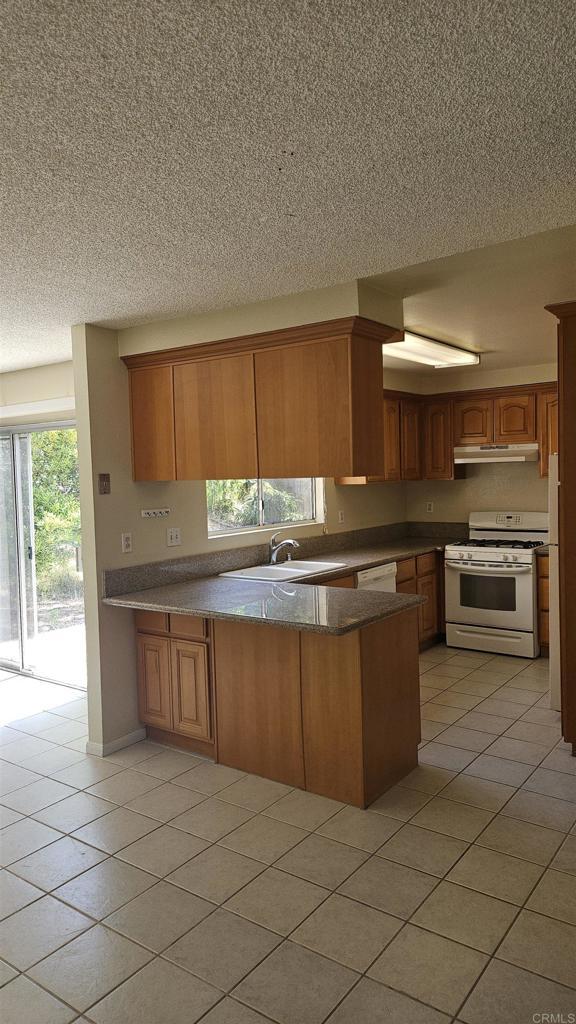 4028 Johnson Dr, Oceanside, CA 92056 - kitchen featuring white appliances, under cabinet range hood, a peninsula, light tile patterned floors, and a textured ceiling