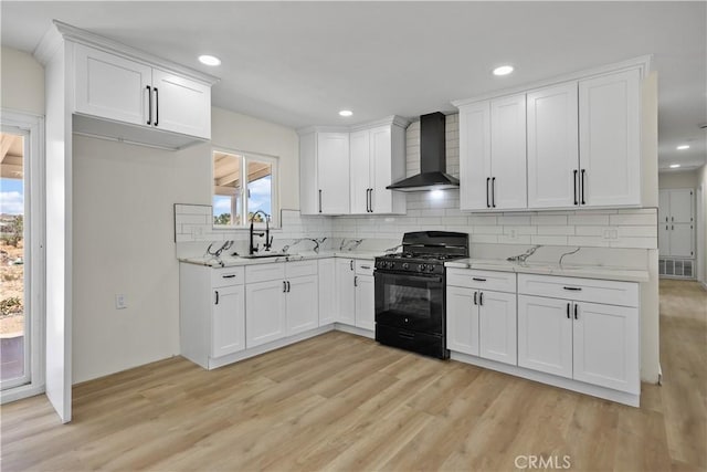 40635 159th St E, Lancaster, CA 93535 - kitchen featuring wall chimney exhaust hood, black gas range oven, light wood-type flooring, backsplash, and white cabinetry