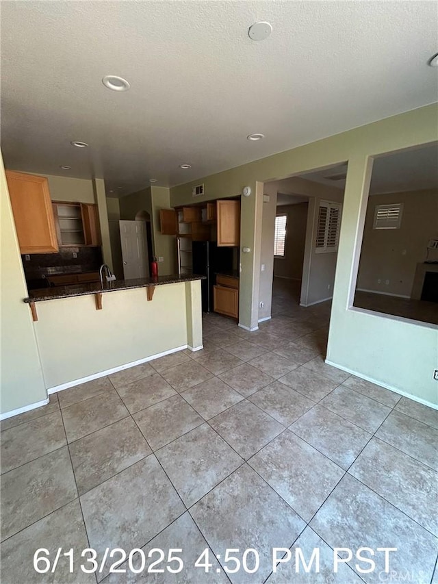 6921 Montego St, Chino, CA 91710 - kitchen featuring a peninsula, dark countertops, a breakfast bar area, light tile patterned floors, and a textured ceiling