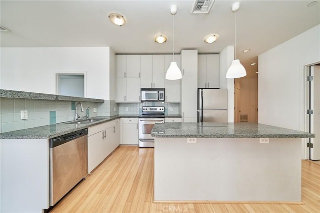 3810 Wilshire Blvd Unit 805, Los Angeles, CA 90010 - kitchen featuring appliances with stainless steel finishes, a kitchen island, light wood-style flooring, tasteful backsplash, and white cabinets