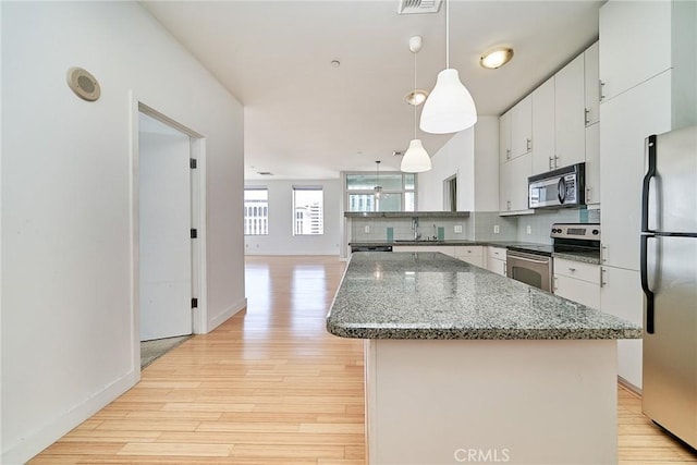 3810 Wilshire Blvd Unit 805, Los Angeles, CA 90010 - kitchen featuring appliances with stainless steel finishes, light wood-style floors, a kitchen island, backsplash, and pendant lighting