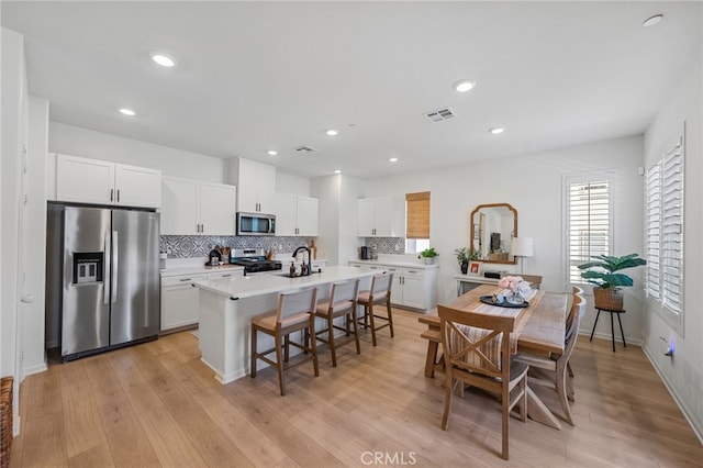 1060 Kendale Way, Vista, CA 92081 - kitchen with appliances with stainless steel finishes, a breakfast bar, a center island with sink, decorative backsplash, and white cabinets