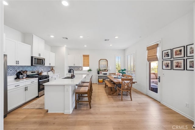 1060 Kendale Way, Vista, CA 92081 - kitchen featuring appliances with stainless steel finishes, backsplash, white cabinets, a kitchen breakfast bar, and light countertops