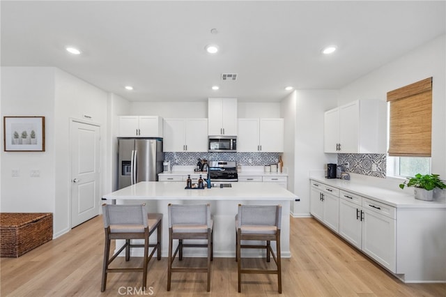 1060 Kendale Way, Vista, CA 92081 - kitchen with stainless steel appliances, a kitchen breakfast bar, decorative backsplash, an island with sink, and light wood-type flooring