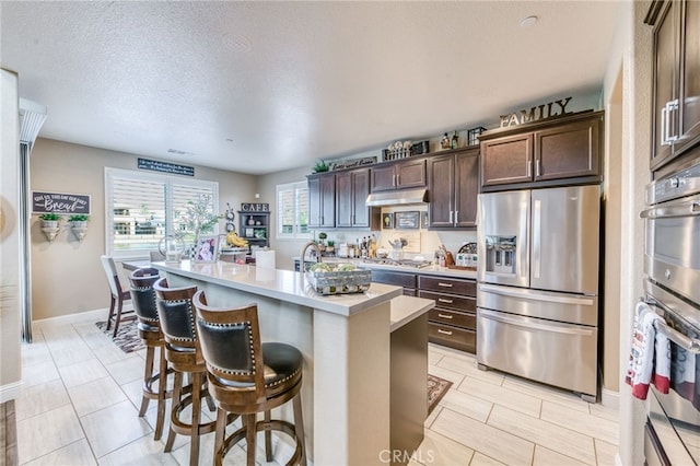 14655 Spanish Bay Way, Chowchilla, CA 93610 - kitchen with stainless steel appliances, dark brown cabinets, light countertops, a kitchen bar, and a kitchen island with sink
