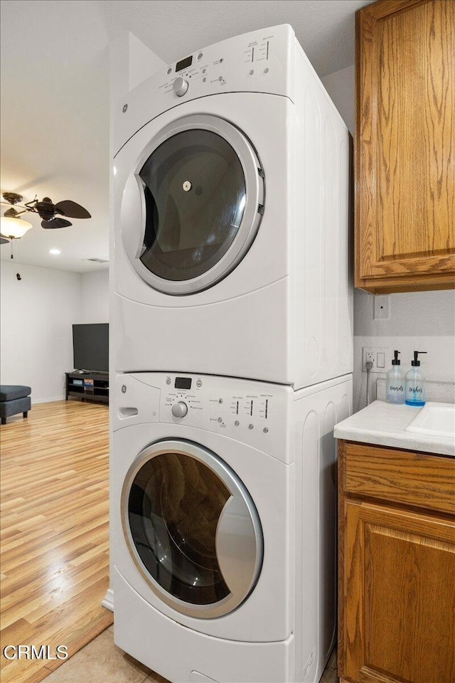 1140 W Lancaster Blvd, Lancaster, CA 93534 - washroom featuring estacked washer and dryer, a ceiling fan, light wood-type flooring, and cabinet space