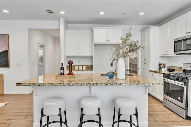 10578 Wells Dr, Rancho Cucamonga, CA 91730 - kitchen with appliances with stainless steel finishes, wood finish floors, white cabinets, a breakfast bar, and a kitchen island with sink