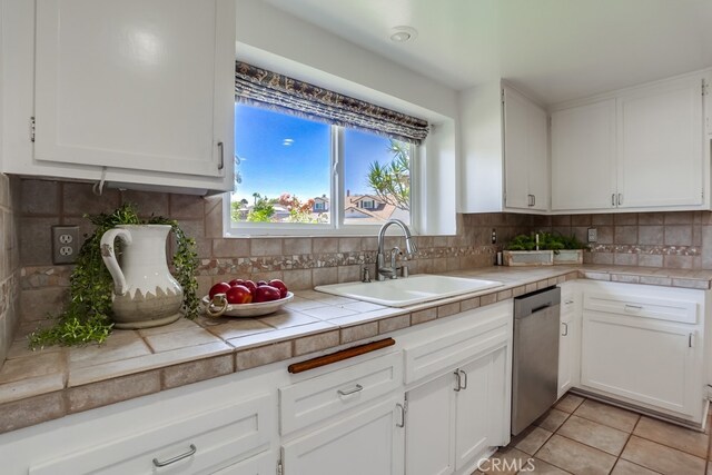 25001 Mackenzie St, Laguna Hills, CA 92653 - kitchen with stainless steel dishwasher, white cabinetry, tile countertops, decorative backsplash, and light tile patterned floors