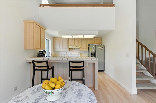 39239 Walnut Ter, Fremont, CA 94536 - kitchen featuring stainless steel fridge with ice dispenser, under cabinet range hood, light brown cabinets, a peninsula, and light wood-style floors
