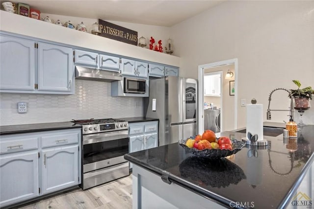 3105 Whisper Oak Way, Bakersfield, CA 93311 - kitchen with appliances with stainless steel finishes, separate washer and dryer, under cabinet range hood, backsplash, and light wood-style flooring